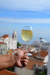 Hand with glass of cold white Portuguese wine in outdoor cafe at view point on old part of Lisbon city, Portugal