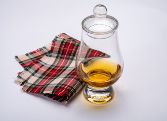 Tulip-shaped tasting glass with dram of Scotch single malt or blended whisky on white background with tartan