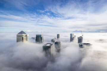 The modern skyline of Canary Wharf, London, during a foggy day with the tops of the skyscrapers...