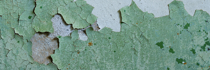 Peeling paint on the wall. Panorama of a concrete wall with old cracked flaking paint. Weathered rough painted surface with patterns of cracks and peeling. Wide panoramic grunge texture for background