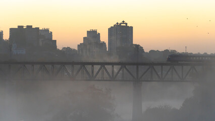 railway bridge in the fog. Train movement on the bridge over the river during fog on the background of sunrise