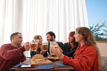 Group of young people having lunch on the terrace home having fun and toasting with beer .