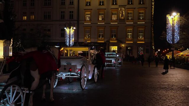 White horse-drawn carriages passing by at night on the street of the city of Krakow with Christmas illumination. Night Krakow on the eve of Christmas and New Year. Authentic traditions of Poland
