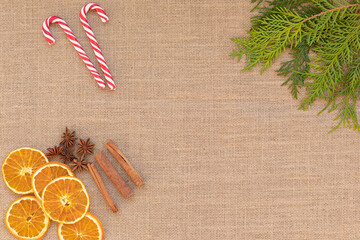 Christmas composition Beautiful top view flat lay arrangement of dry Oranges, cinnamon sticks, star anise and Christmas candy canes on burlap fabric background.