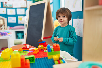 Adorable toddler playing with construction blocks standing at kindergarten