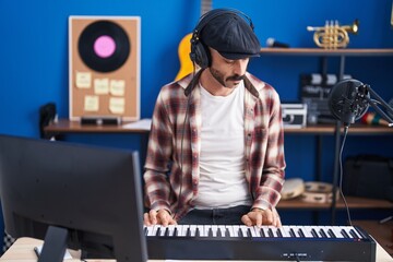 Young hispanic man musician playing piano keyboard at music studio