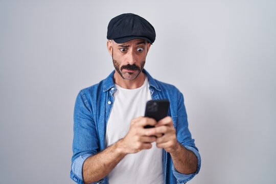 Hispanic man with beard using smartphone typing message skeptic and nervous, frowning upset because of problem. negative person.