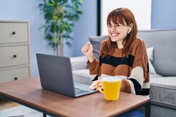 Young beautiful woman using computer laptop doing video call screaming proud, celebrating victory and success very excited with raised arm