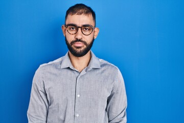 Obraz premium Middle east man with beard standing over blue background relaxed with serious expression on face. simple and natural looking at the camera.