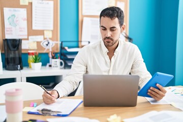 Young hispanic man business worker using touchpad writing on document at office