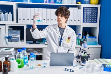 Young hispanic man scientist using laptop measuring liquid at laboratory