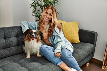 Young caucasian woman smiling confident sitting on sofa with dog at home