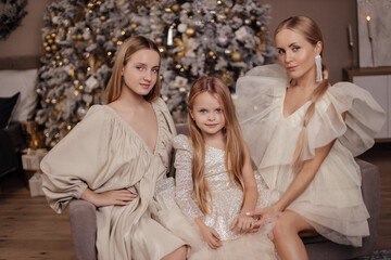 mother and her daughters with blond hair in elegant dresses posing in decorated studio with...
