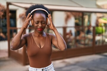 African woman with curly hair outdoors at the city wearing headphones depressed and worry for...