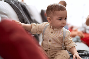 Adorable toddler sitting on sofa with serious expression at home