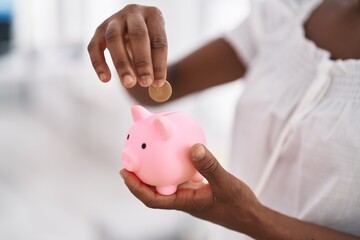 African american woman inserting coin on piggy bank at home