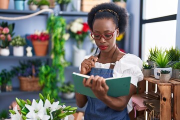 African american woman florist reading notebook with doubt expression at florist store
