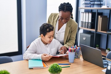 African american mother and son using laptop and reading book at office