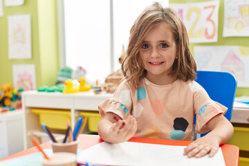 Adorable hispanic girl student drawing on paper sitting on table at kindergarten
