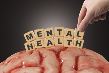 The hand touches wooden blocks with the inscription Mental Health on the background of the brain....
