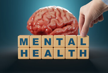 The hand touches wooden blocks with the inscription Mental Health on the background of the brain. The concept of mental problems, mental illness. Taking care of your mental health.