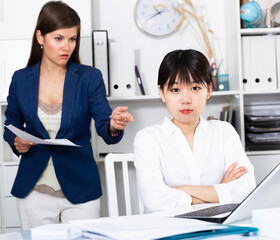 Portrait of young stressed asian businesswoman in multiracial office with dissatisfied female chief...
