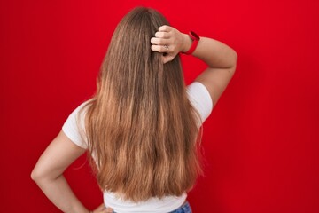 Young caucasian woman standing over red background backwards thinking about doubt with hand on head