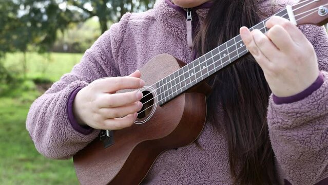 Unrecognizable female person happily playing ukelele standing on the grass.