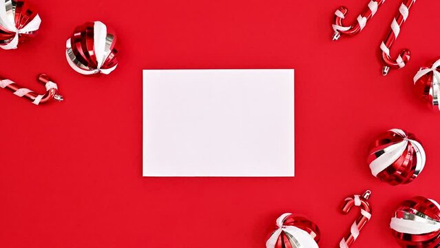Christmas greeting card with paper come from envelope on red background with Christmas ornaments. Stop motion 
