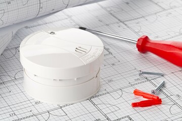 Smoke detector or fire alarm sensor on white architectural plans background with tools, house...