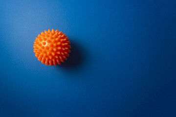 Orange massage ball as myofascial release equipment for trigger points on dark blue background. Minimal concept of MFR, self-massage and physiotherapy. Selective focus, copy space