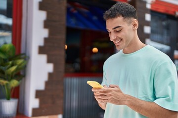 Young hispanic man smiling confident using smartphone at street