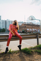 Young adult model with cool glasses and outfit posing for camera with a basketball field in the background