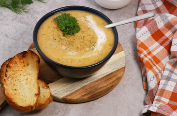 red lentils soup puree in dark bowl with bread on grey marble table