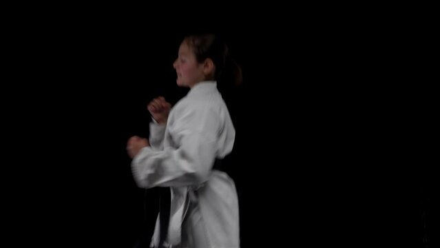 Young girl wearing kimono and practicing karate against black background