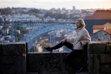 Fototapeta premium A woman sits on a stone wall in the center of Porto, Portugal.