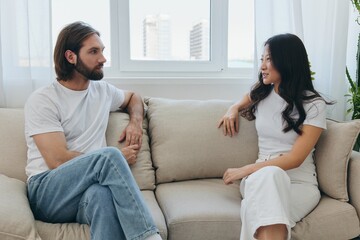 Male and female Asian friends sitting on the couch and having fun talking to each other with a smile having a good time together. Lifestyle in happiness at home