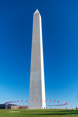 Lots of united states flags against a blue sky, at the base of George Washington Memorial in Washington D.C.