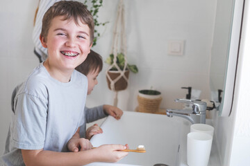Happy boy child cleaning teeth with braces use wooden eco friendly toothbrush healthy lifestyle