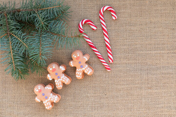 Flat lay Christmas and New Year composition. Gingerbread men, Christmas candy canes. branch of Christmas tree on burlap fabric background, space for text