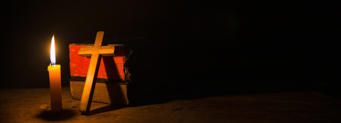 Light candle with holy bible and cross or crucifix on old wooden background in church.Candlelight...