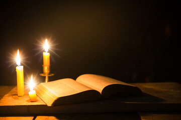 Light candle with holy bible and cross or crucifix on old wooden background in church.Candlelight...