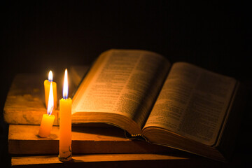 Light candle with holy bible and cross or crucifix on old wooden background in church.Candlelight...