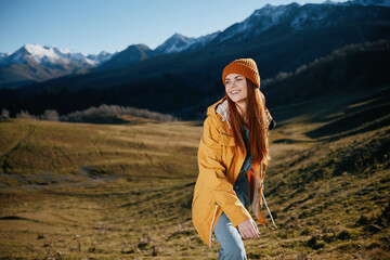 Naklejka premium Woman standing beautifully on a hill smile with teeth in the mountains in the autumn in a yellow raincoat and jeans happy sunset trip to hike the mountains in the snow, freedom lifestyle 