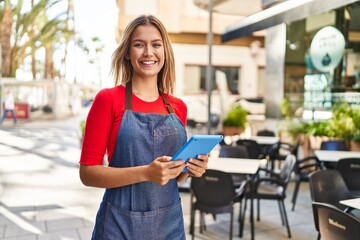 Young hispanic woman waitress smiling confident using touchpad at coffee shop terrace