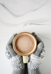 Gloves holding mug of hot chocolate