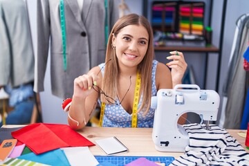 Young beautiful hispanic woman tailor smiling confident holding glasses at tailor shop