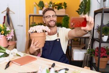 Middle age man florist make selfie by smartphone holding plant at flower shop