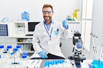 Middle age man working at scientist laboratory smiling happy and positive, thumb up doing excellent and approval sign