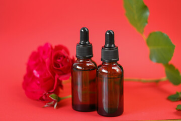 Rose essential oil. Organic rose oil in brown glass bottles set and red rose on red background.Aromatherapy and cosmetics concept.Organic natural rose oil.Organic bio cosmetics
